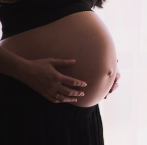 Closeup of a pregnant woman holding her exposed belly