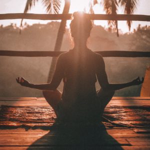 Woman meditating in the sun holding a Gyan mudra yoga pose (cross legged with thumb and index finger together on both hands).