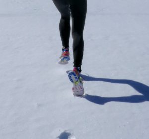 A person's legs running in the snow, leaving behind footprints.