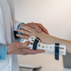 A close-up of a doctor in a white coat putting a brace on a patient's wrist.