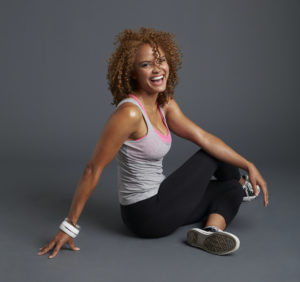 A woman sitting on the floor in workout clothes while smiling at the camera