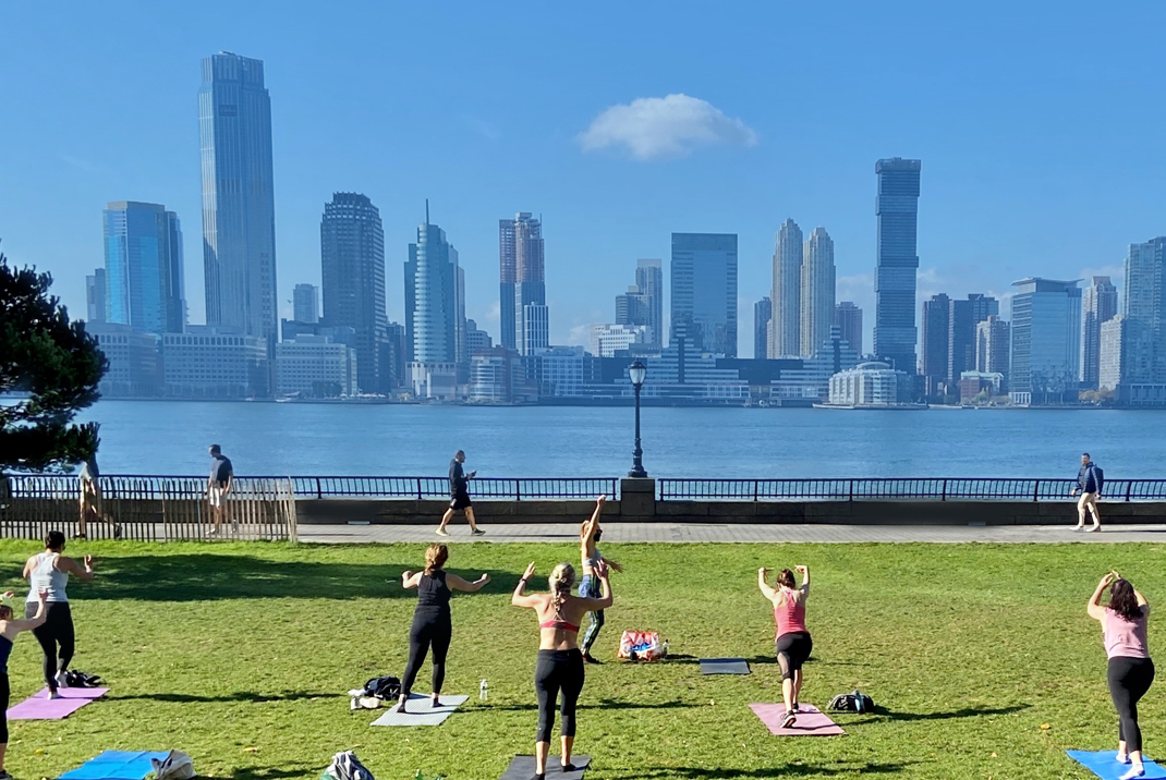 A group of people doing an outdoor workout on yoga mats while facing the NYC skyline