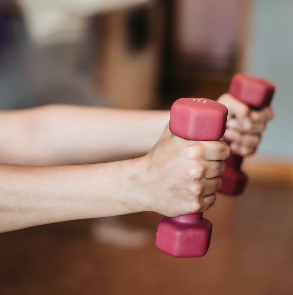 Closeup of a person doing a workout routine with their arms outretched while holding pink dumbbells.