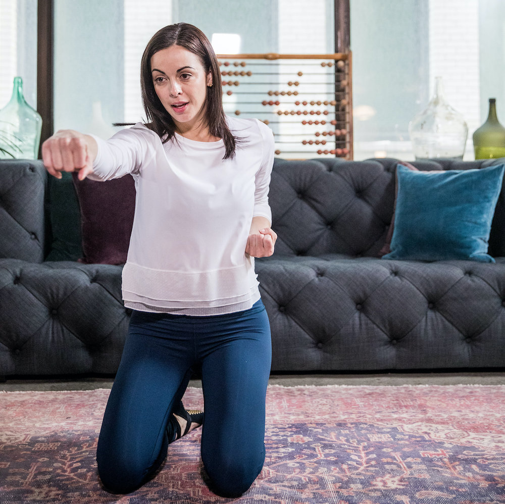 A woman kneeling on her living room floor while punching the air during an at home workout