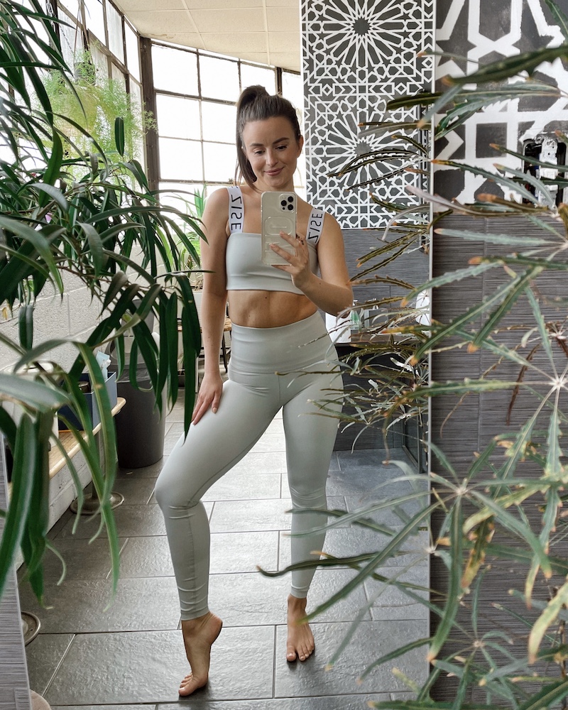 Woman wearing a mint-colored ZISE workout set taking a full-body selfie in front of a mirror surrounded by house plants