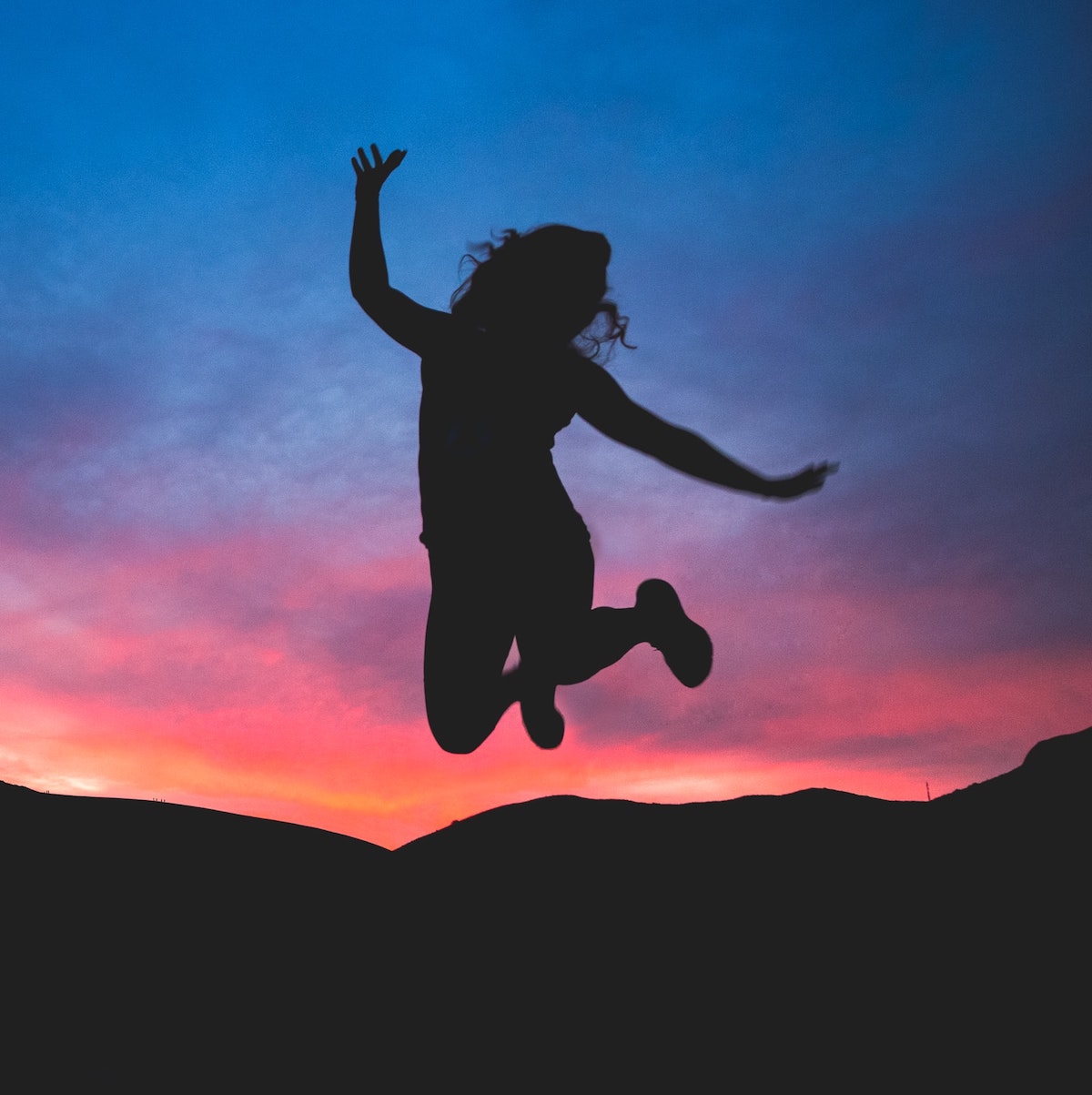 Silhouette of a person jumping in front of a sunset and mountains.
