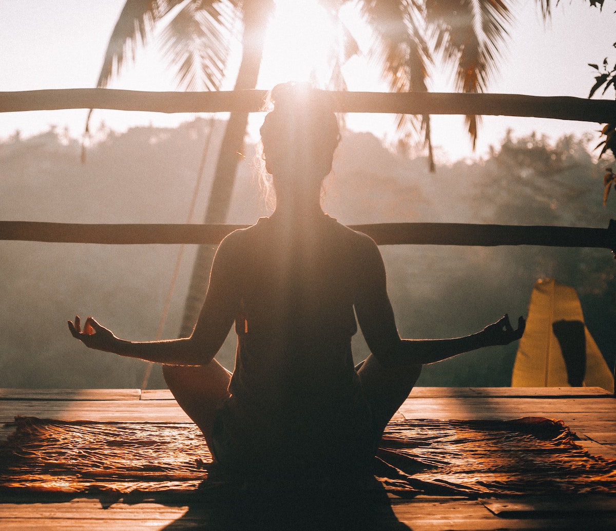Woman meditating in the sun holding a Gyan mudra yoga pose (cross legged with thumb and index finger together on both hands)