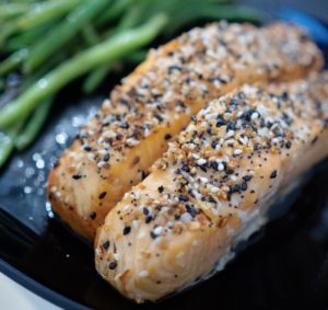Closeup of two pieces of salmon coated in sesame seeds and seasoning sitting on a plate.