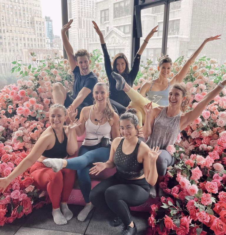 A group of Physique 57 barre instructors smiling at the camera in front of a floral wonderland during the Inspiring Strength Tour