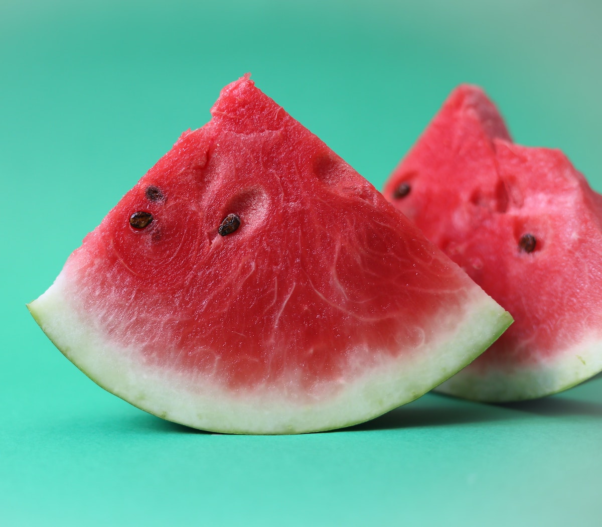 Two slices of watermelon in front of a teal background.