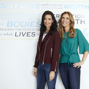 Jennifer Vaughan Maanavi and Tanya Becker, the creators of Physique 57, standing in front of a Physique 57 banner.