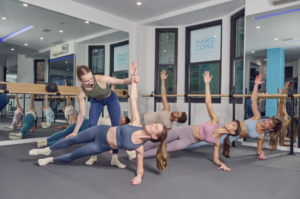 A trainer in a barre class corrects a participant's form.